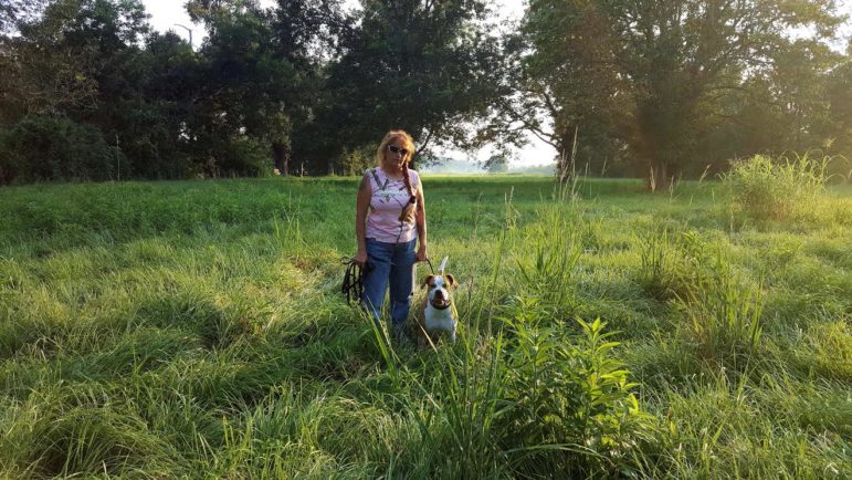 Woman and dog stand in a field 